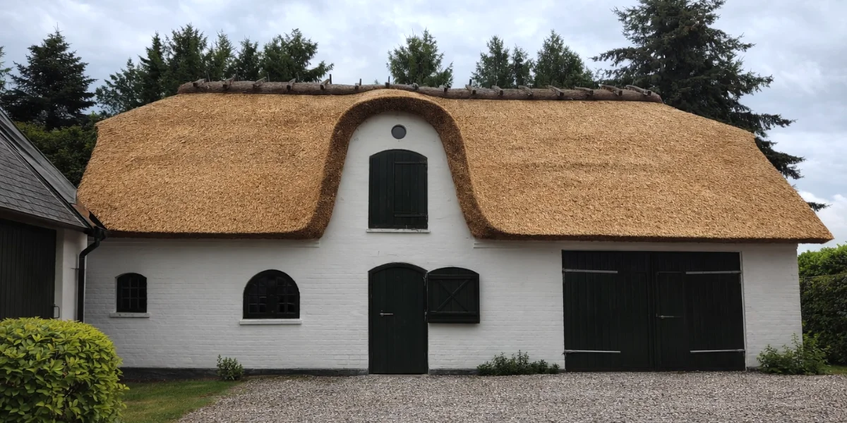 White barn with thick thatched roof and black doors